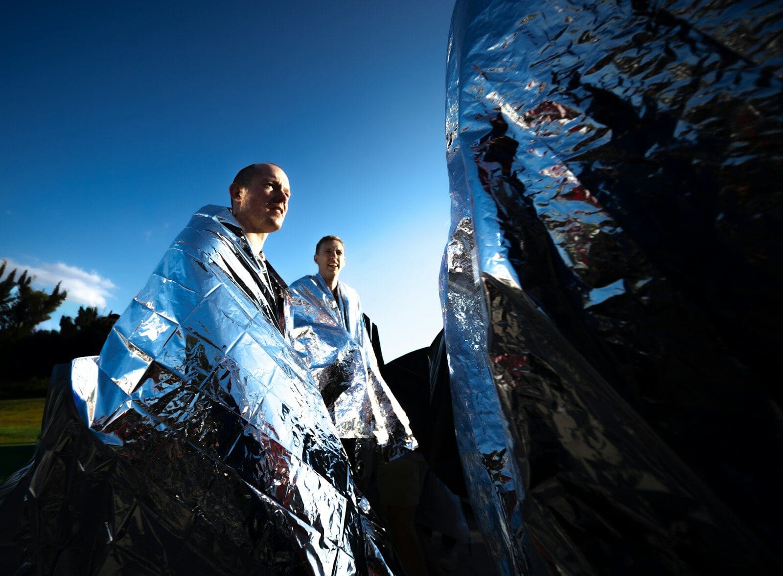 Two people wrapped in shiny emergency blankets outdoors