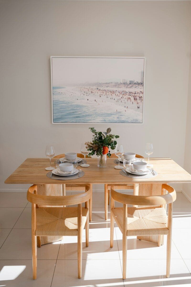 A wooden dining table set for two with beach artwork